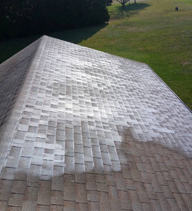 Shingled roof with a bright white patch of repaired or stained shingles on a grassy background