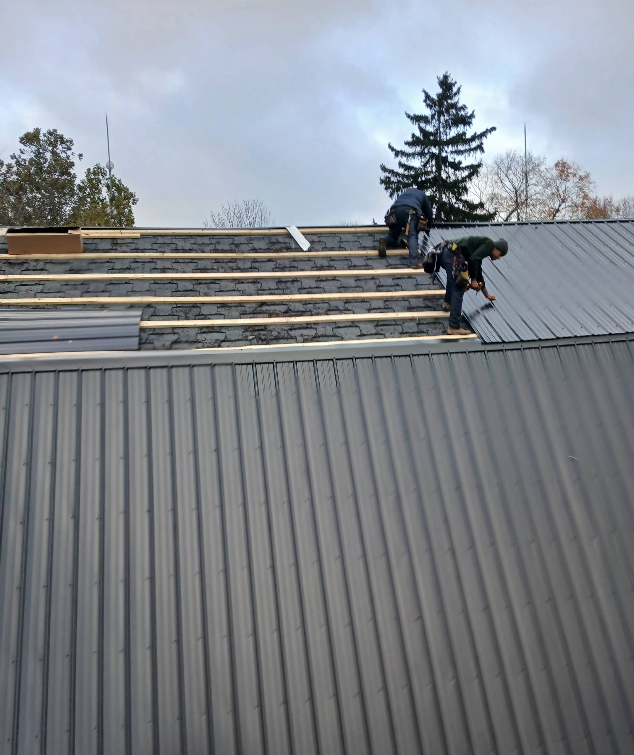 Two workers installing roof panels on a sloped metal roof under a cloudy sky