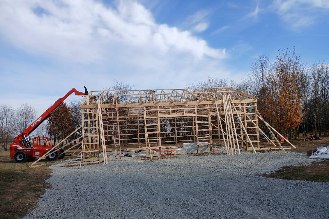 Construction site with a wooden roof frame and a red crane on gravel under a cloudy sky