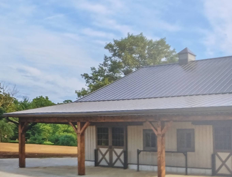 White barn with a gray metal roof and wooden porch posts under a blue sky.