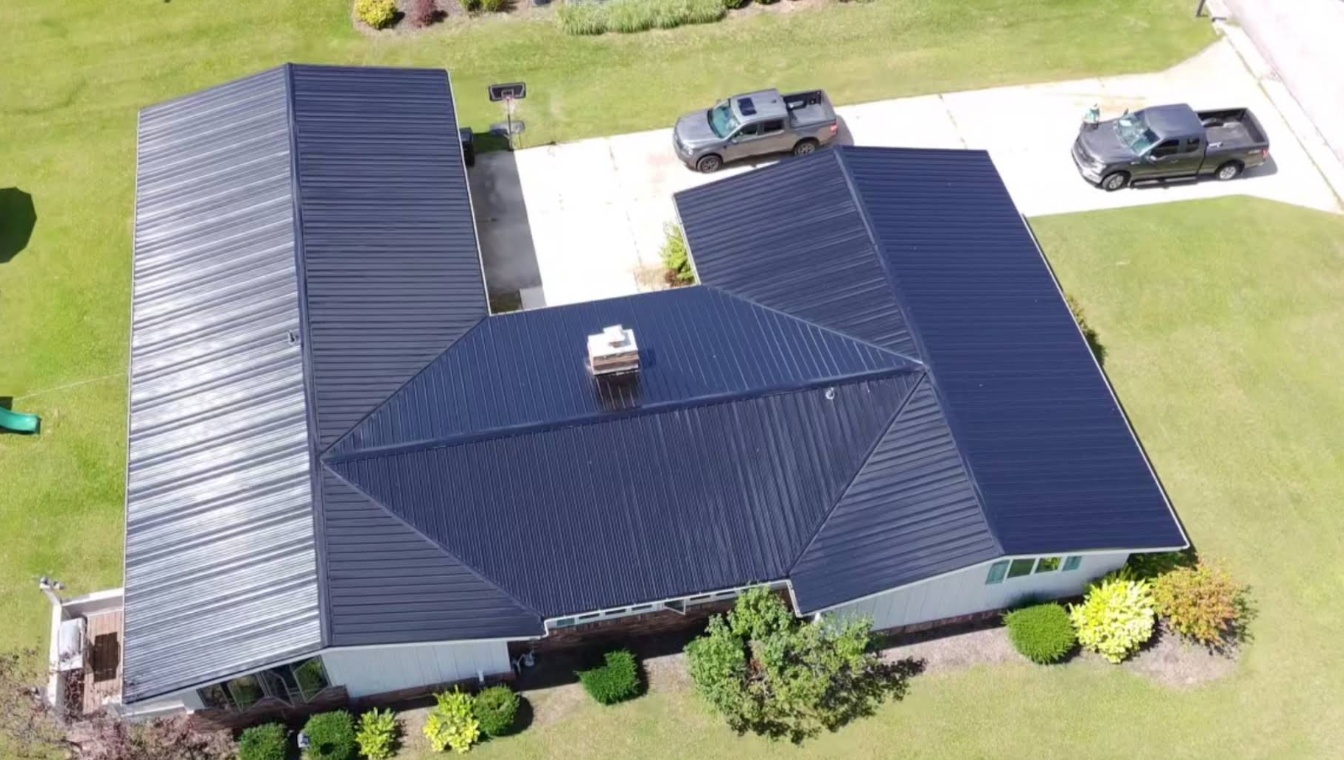 Aerial view of a house with a dark roof, lawn, driveway, and parked car