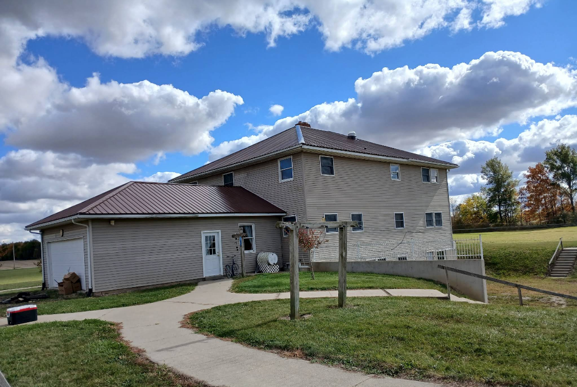 Large beige house with brown roof beside a curved sidewalk under a cloudy blue sky
