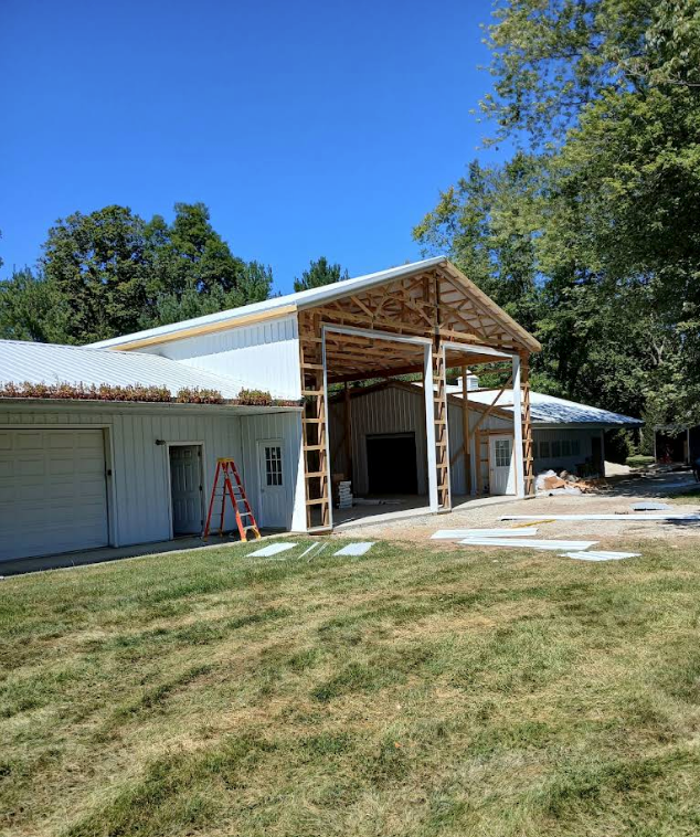 Partially built white house addition with exposed framing and open garage under a blue sky