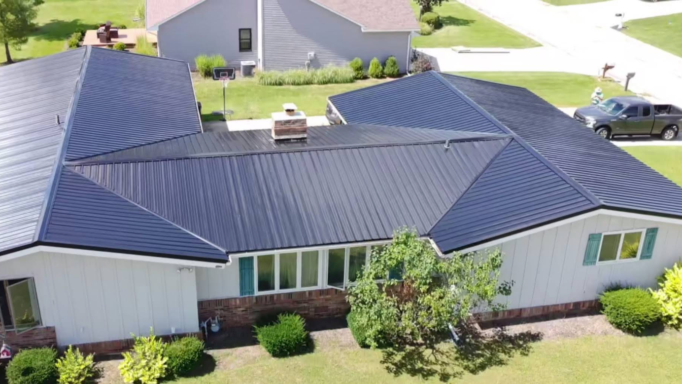 Aerial view of a house with a dark blue roof, white siding, and a small front yard.