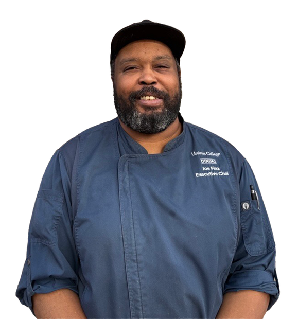 Chef Joe Flax, wearing a cap and chef coat, smiles.