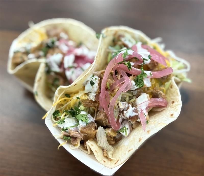 Two soft flour tacos filled with shredded meat, pickled onions, white sauce, and cilantro.