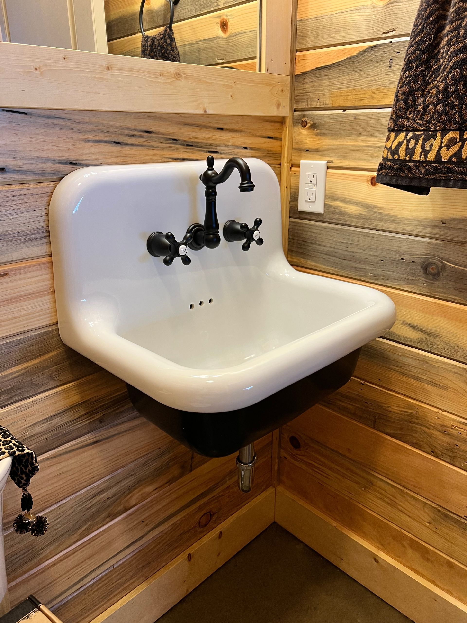 White wall-mounted sink with black faucet in a rustic wood-paneled corner.