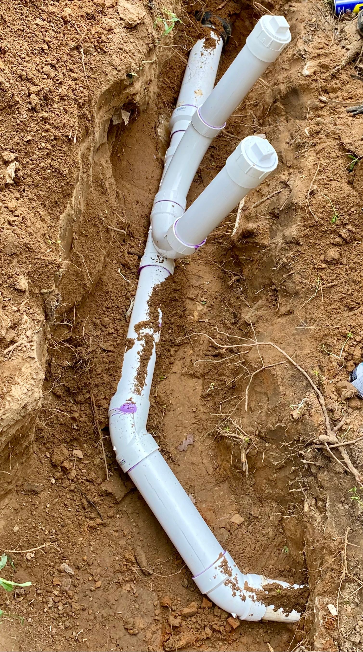 White PVC pipes buried in brown soil, branching in a trench.