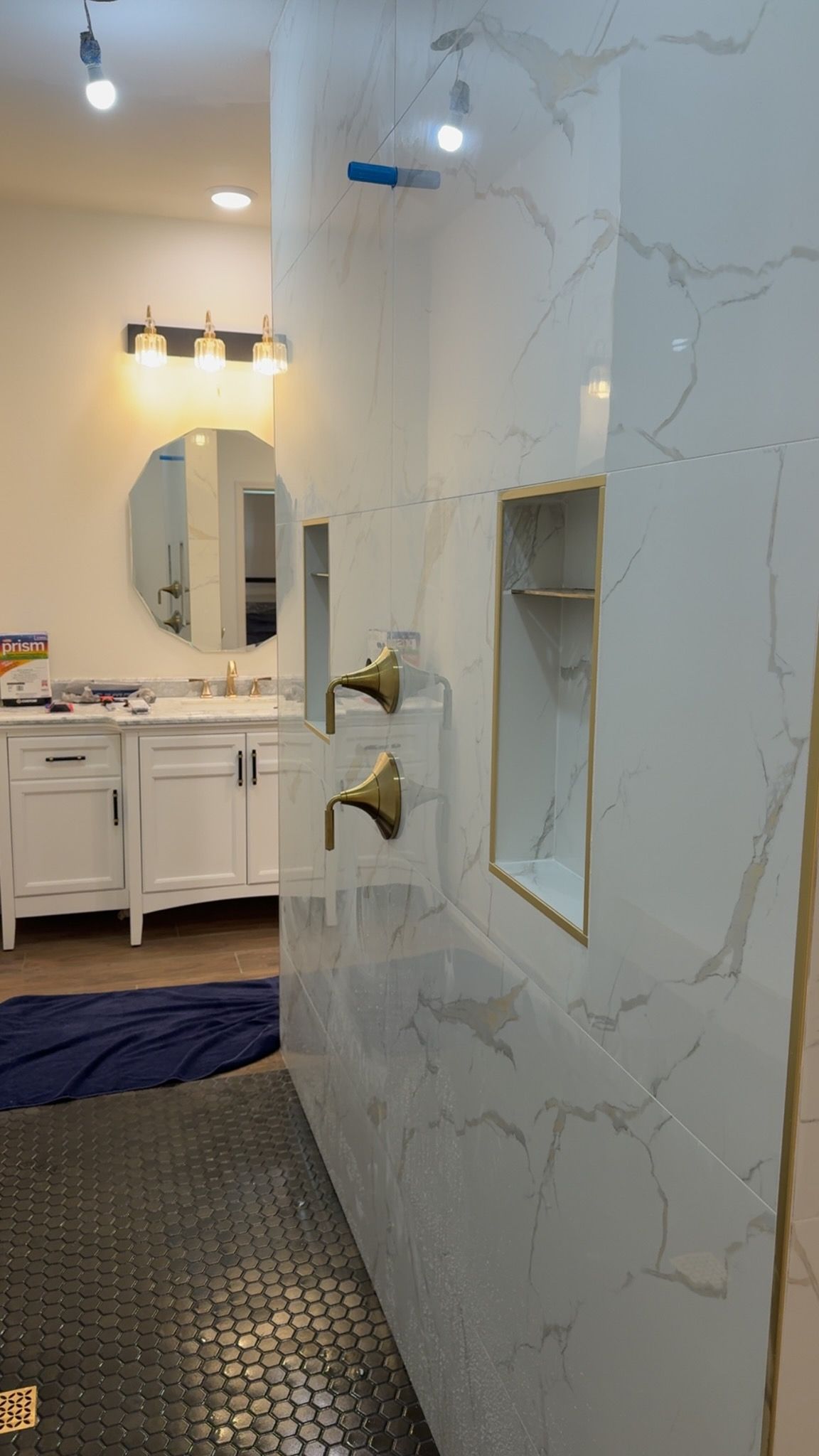 Marble-tiled shower wall with recessed shelves beside a bathroom vanity and mirror.