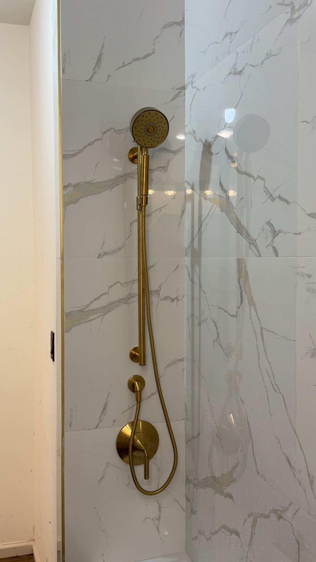 Gold shower fixtures on a white marble-tiled wall in a bathroom.