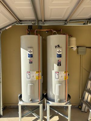 Two white water heaters in a garage under a partially open door.