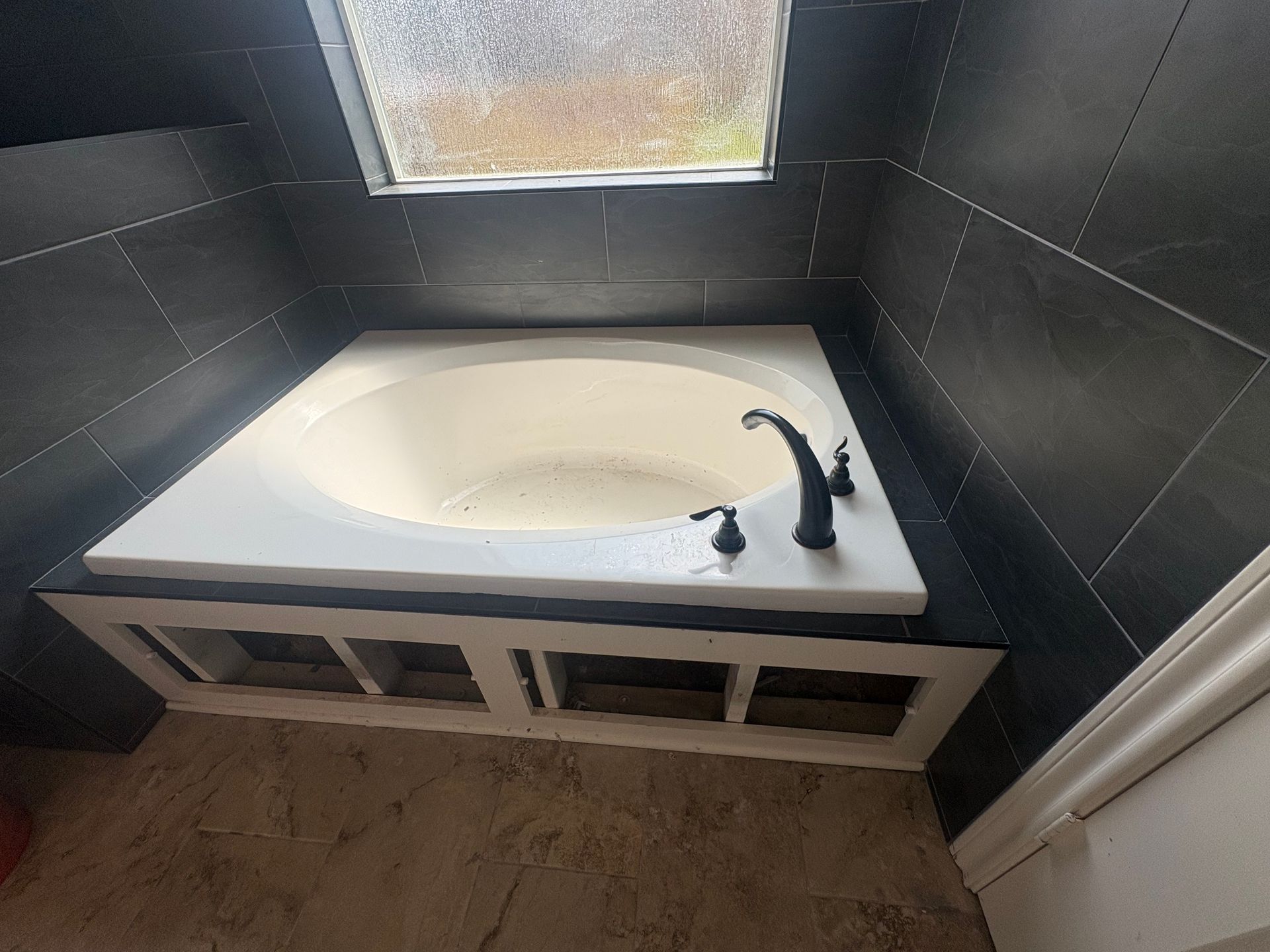 Small bathroom with a white corner tub, black walls, and a window above.