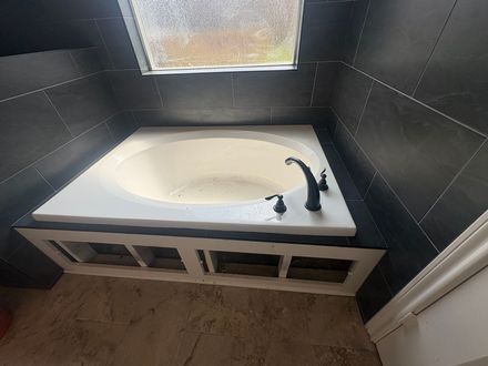 Small bathroom with a white corner tub, black walls, and a window above.