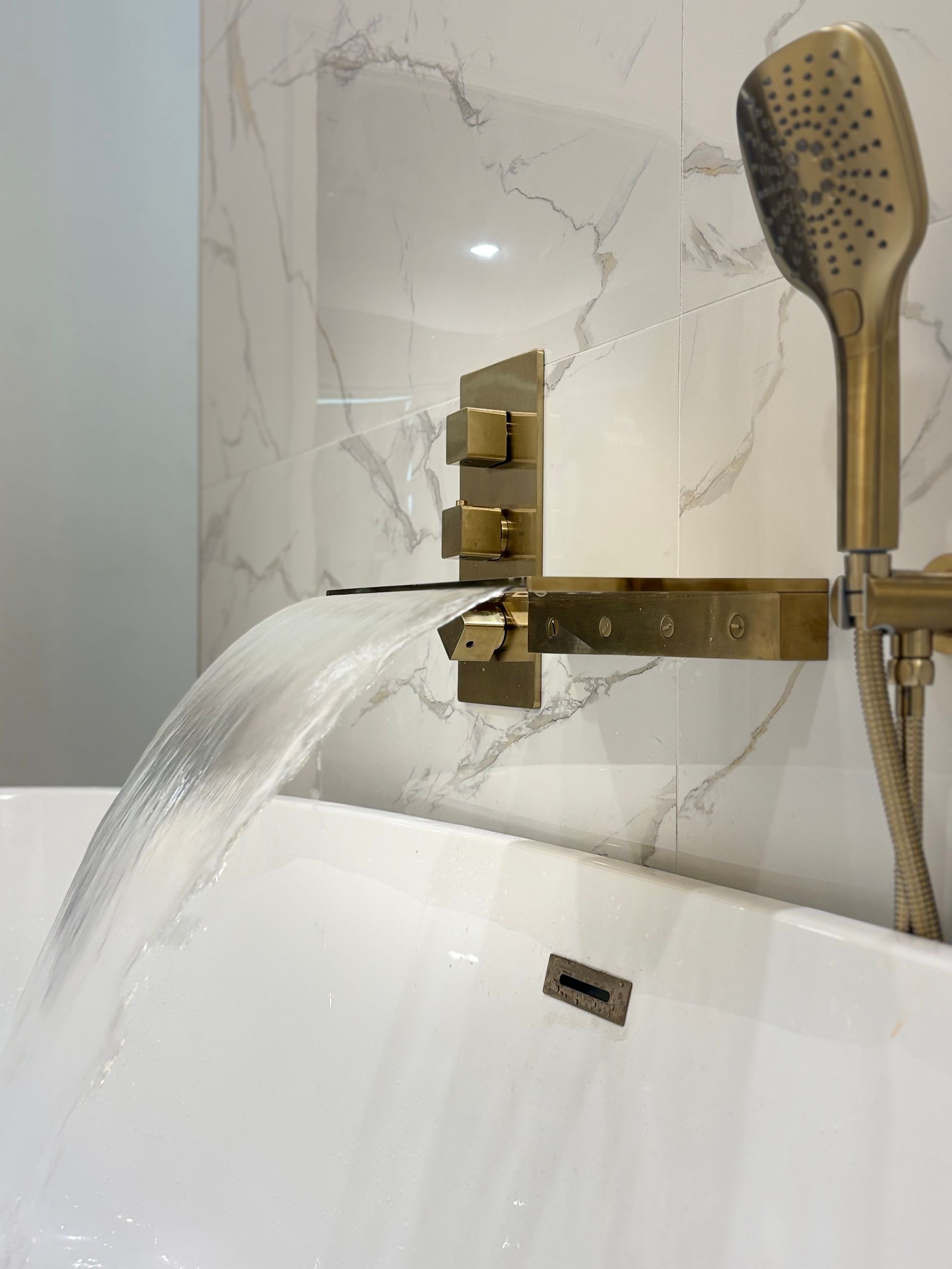 Gold faucet pouring water into a white bathtub, with a handheld shower on the right.