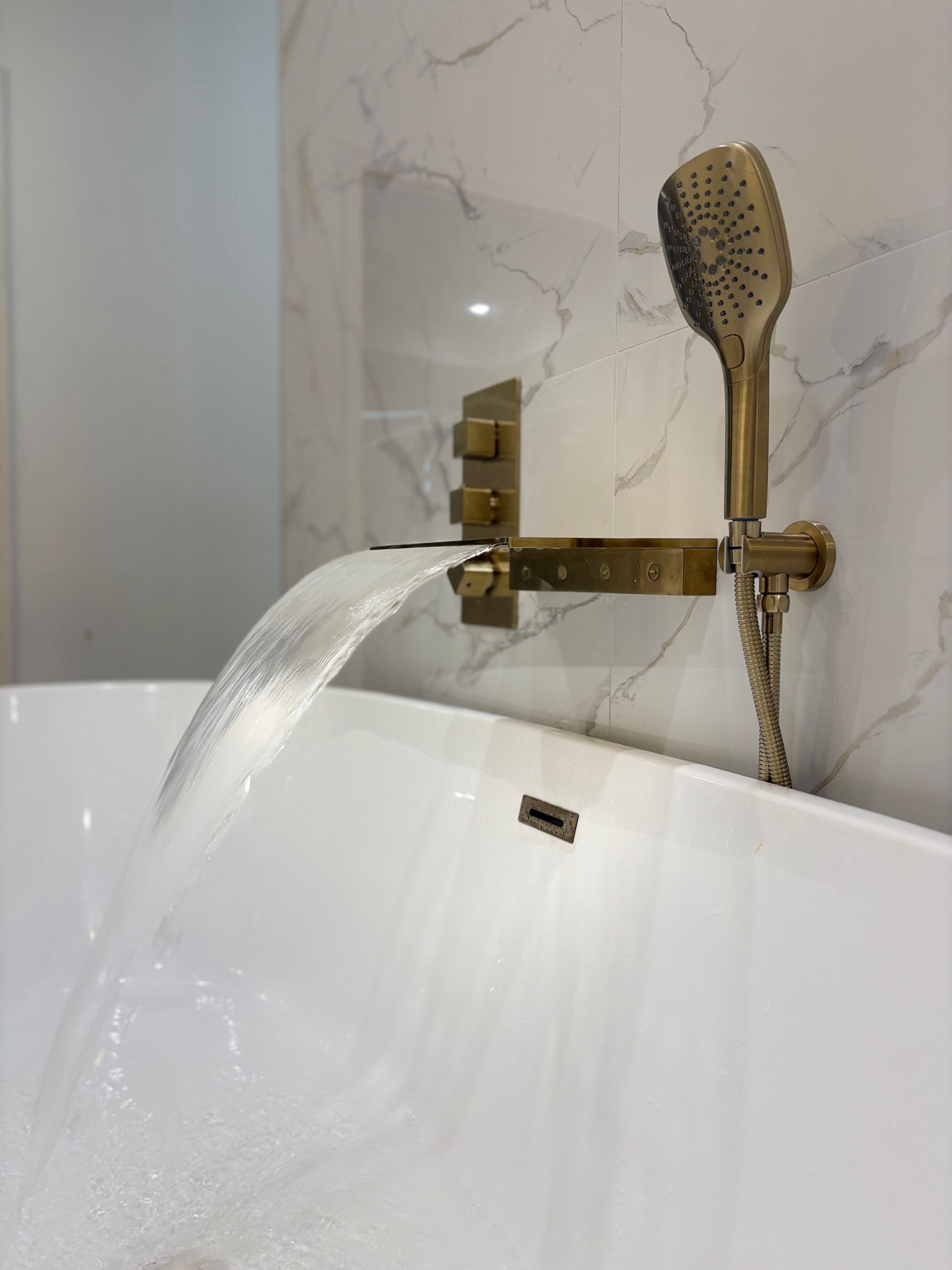 Gold faucet pouring water into a white bathtub with a handheld shower head nearby