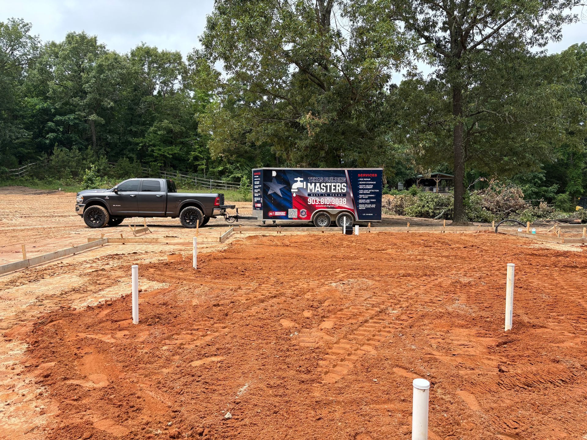 Construction lot with black pickup truck, banner, and white survey stakes on red dirt site