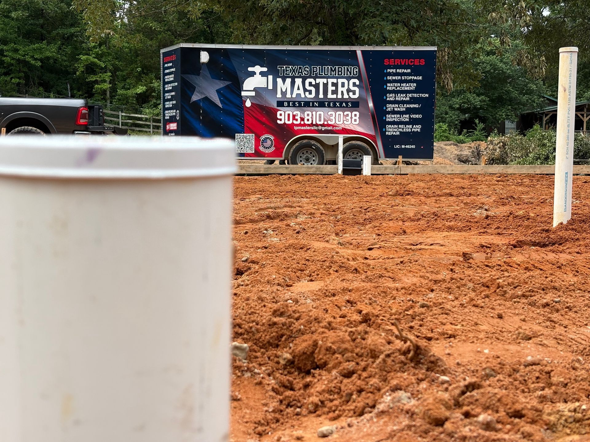 Construction site with red dirt, white pipe, and a blue trailer sign reading “Masters” in the background