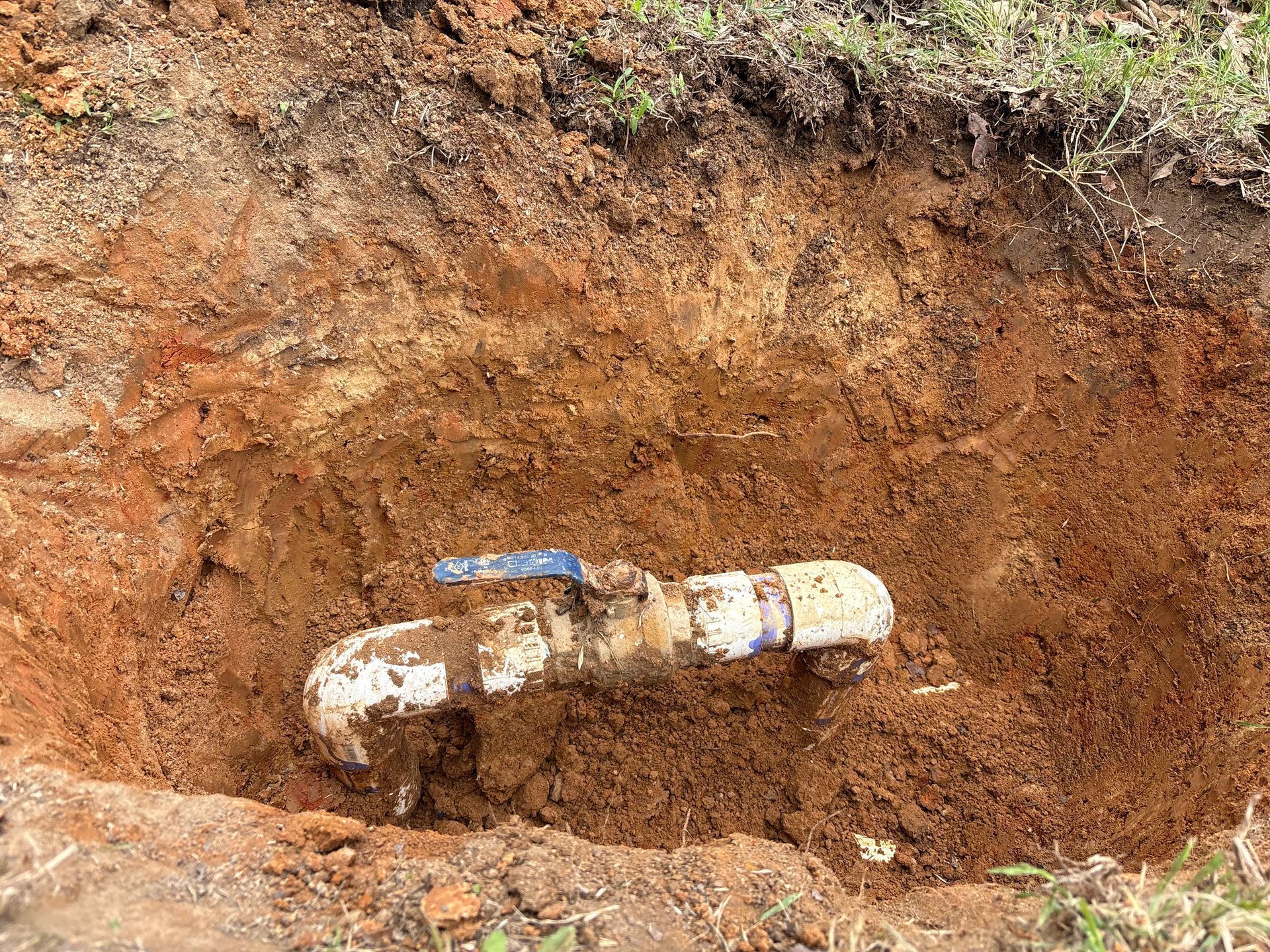 Damaged white pipe with blue valve exposed in a dirt trench