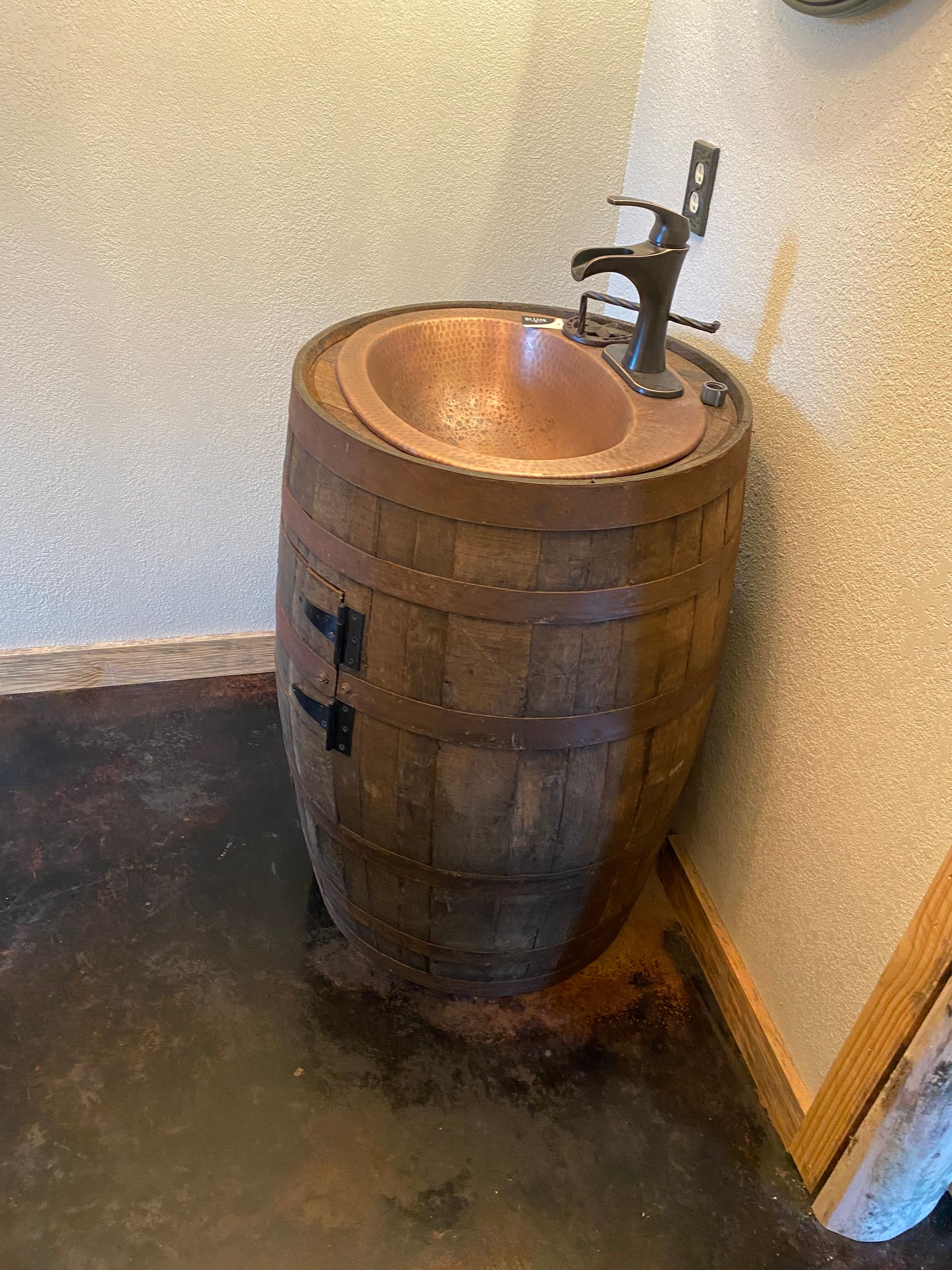 Copper sink set in a wooden barrel vanity against a corner wall.