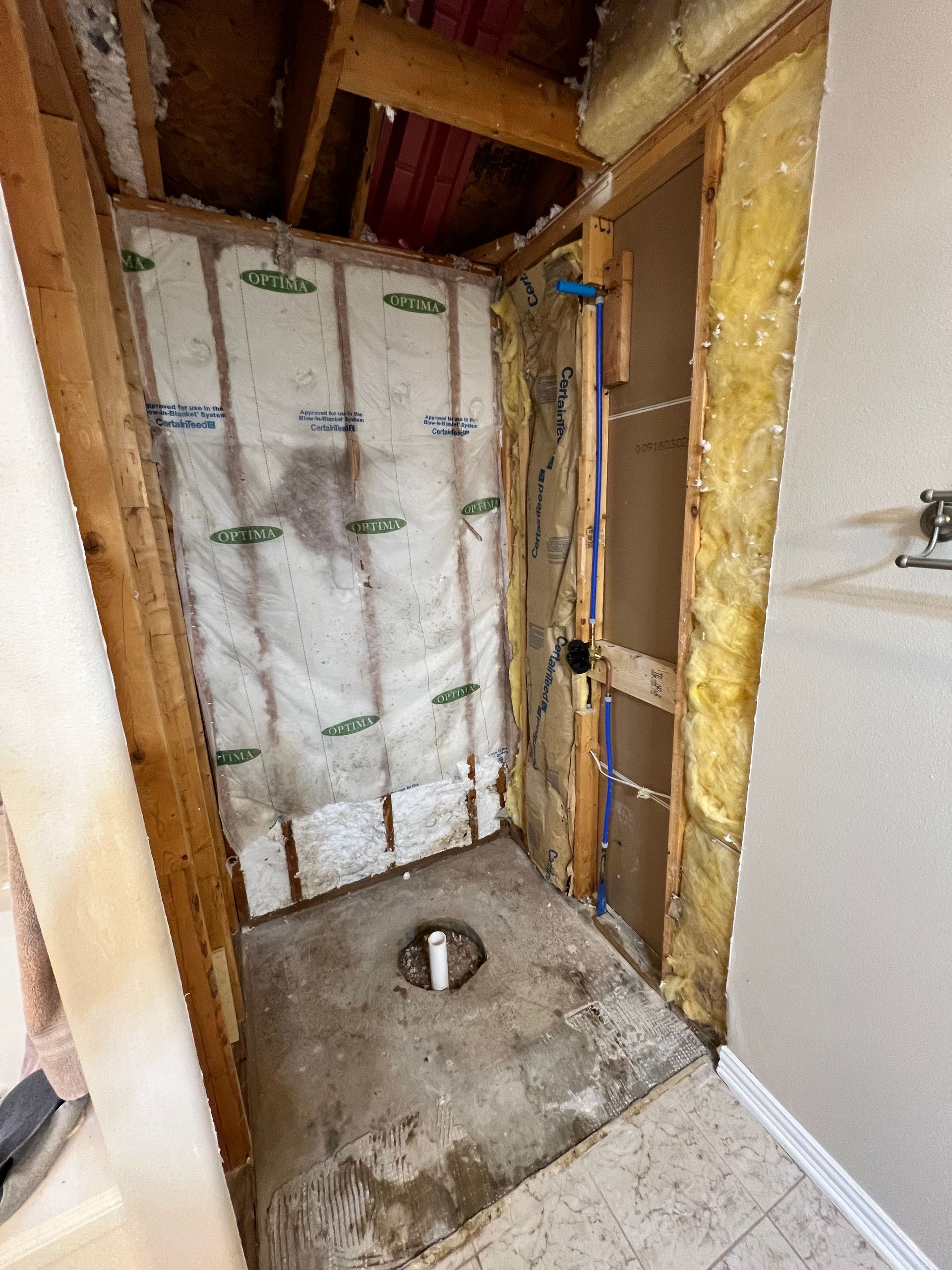 Partially gutted bathroom with exposed insulation, open wall framing, and a floor drain.