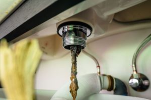 Leak from under-sink pipe with water dripping into a kitchen cabinet
