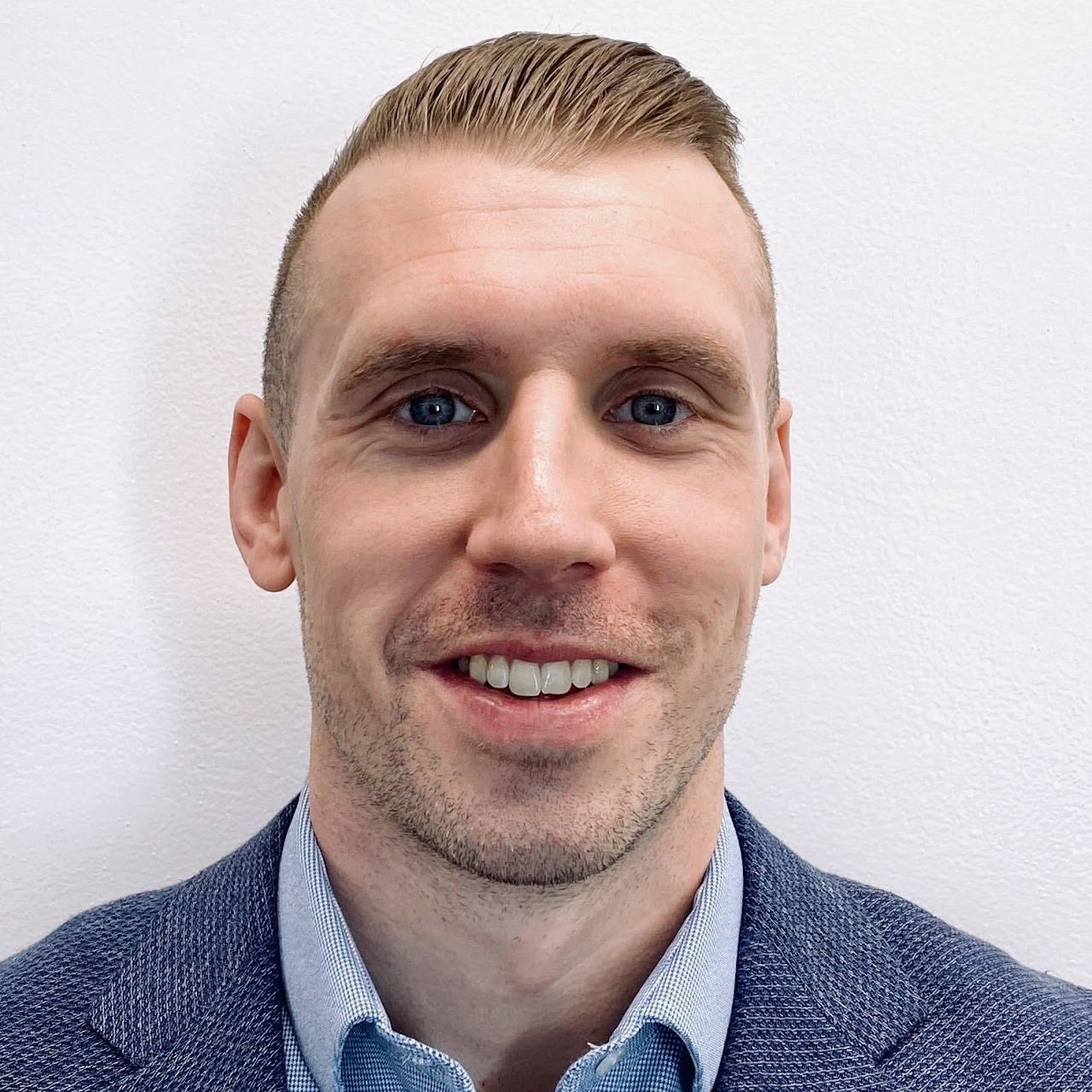 A man in a blue jacket and blue shirt is smiling for the camera