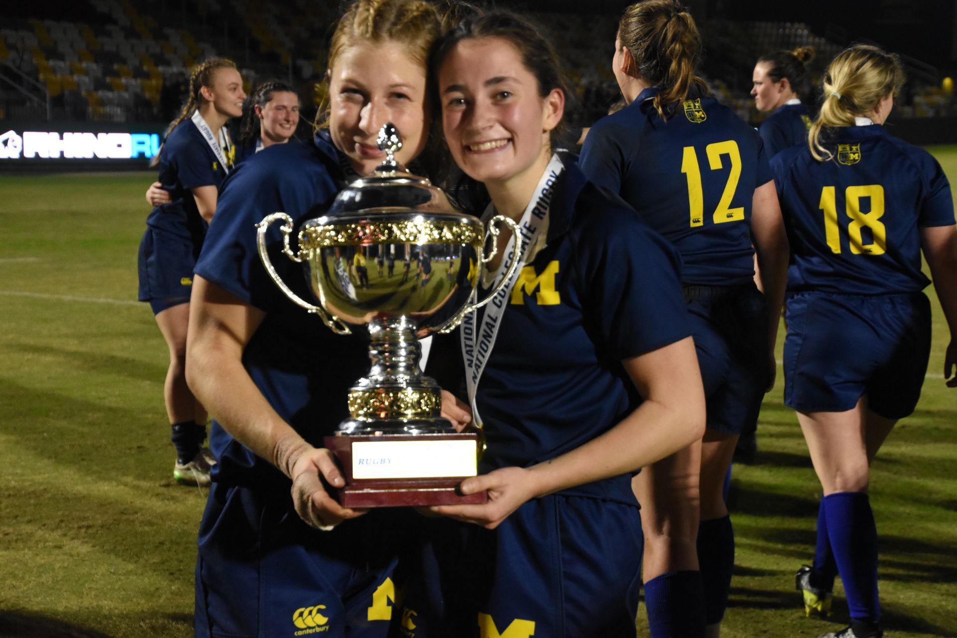 Two girls holding a trophy with the number 12 and 18 on their jerseys