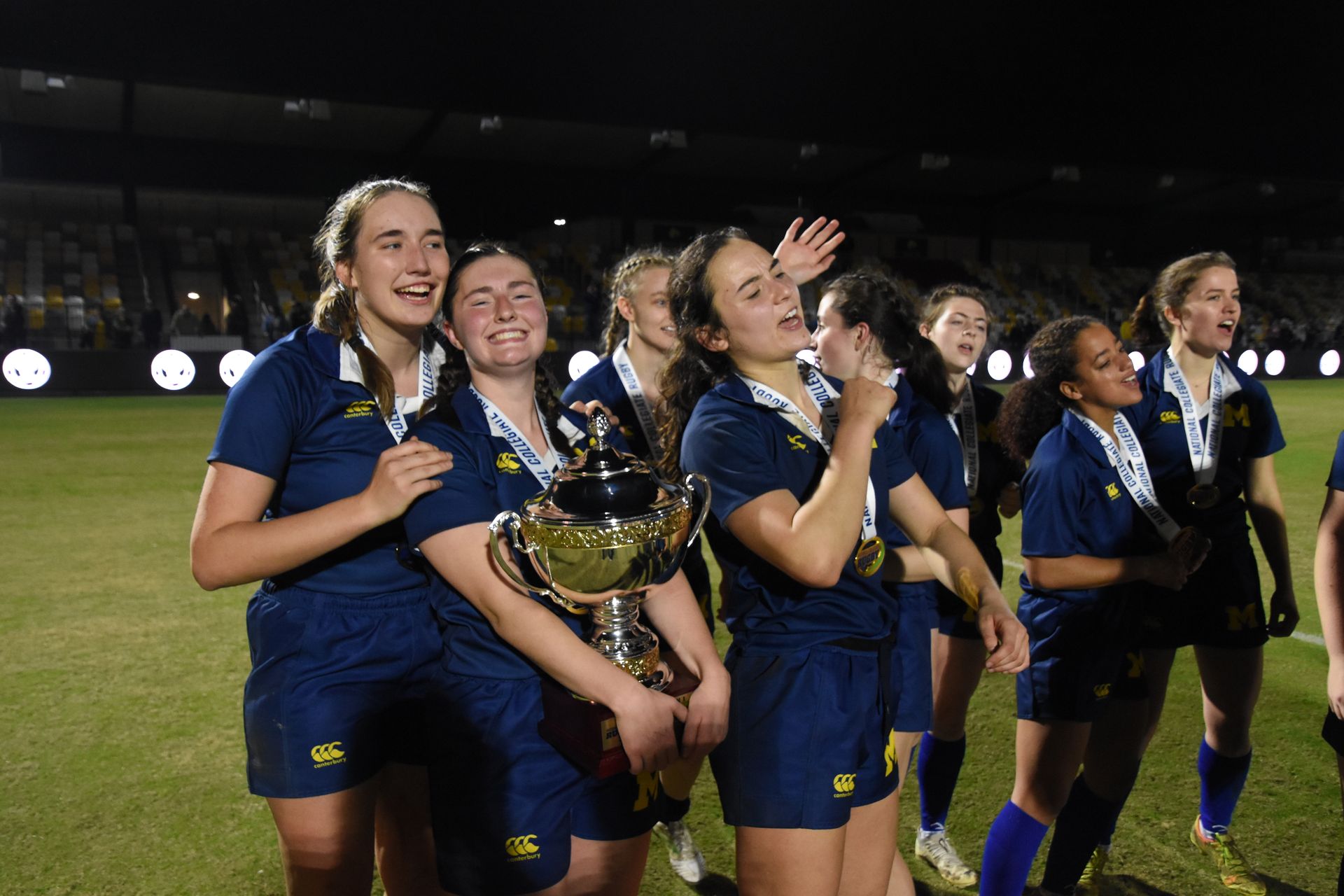 A group of women are standing on a field holding a trophy.