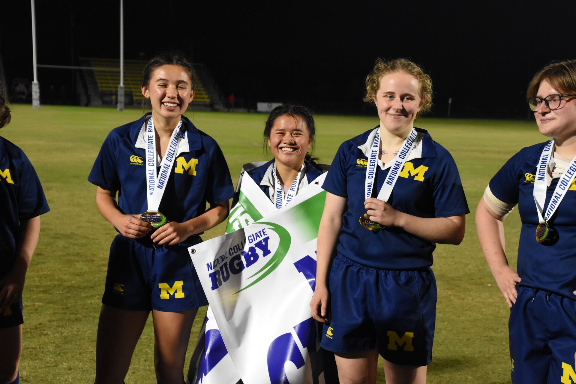 A group of female rugby players are posing for a picture on a field.