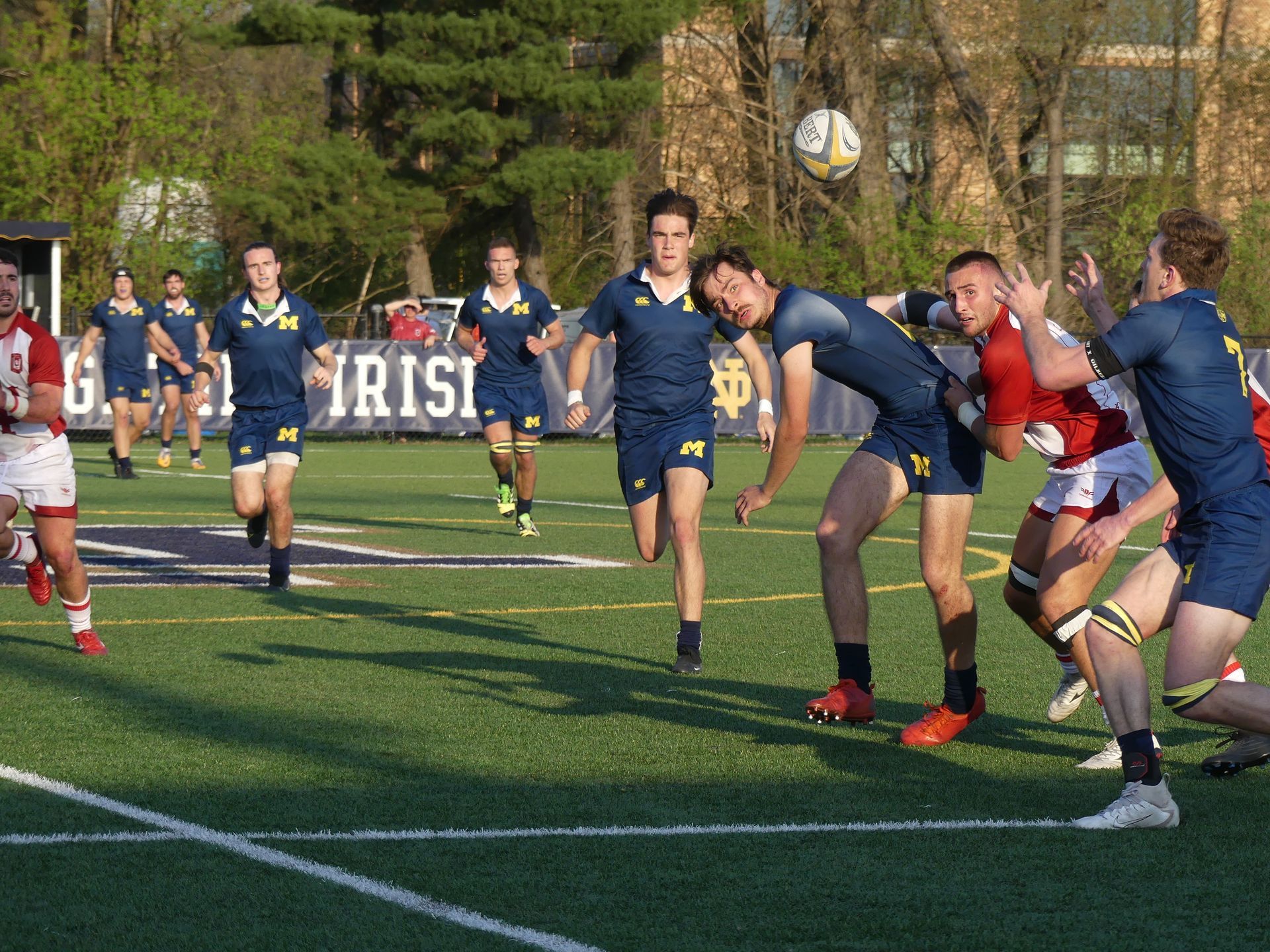 A group of men are playing rugby on a field with a sign that says ' irish ' on it