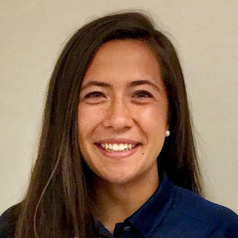 A woman with long hair is smiling and wearing a blue shirt.