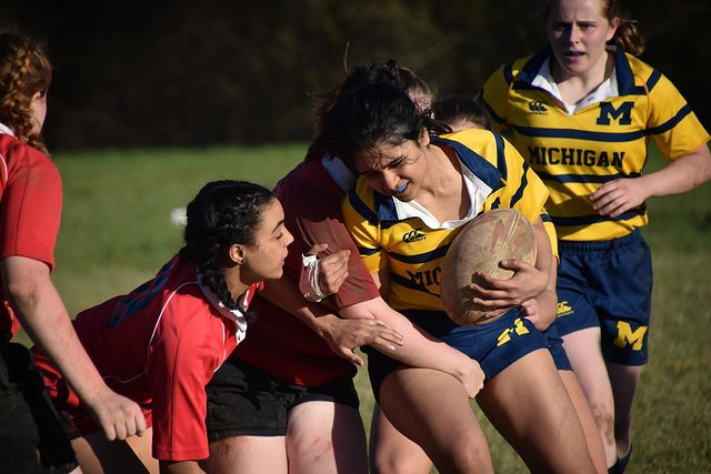 A woman in a michigan jersey is holding a rugby ball