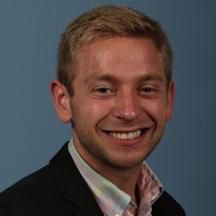 A man in a suit and pink shirt is smiling for the camera