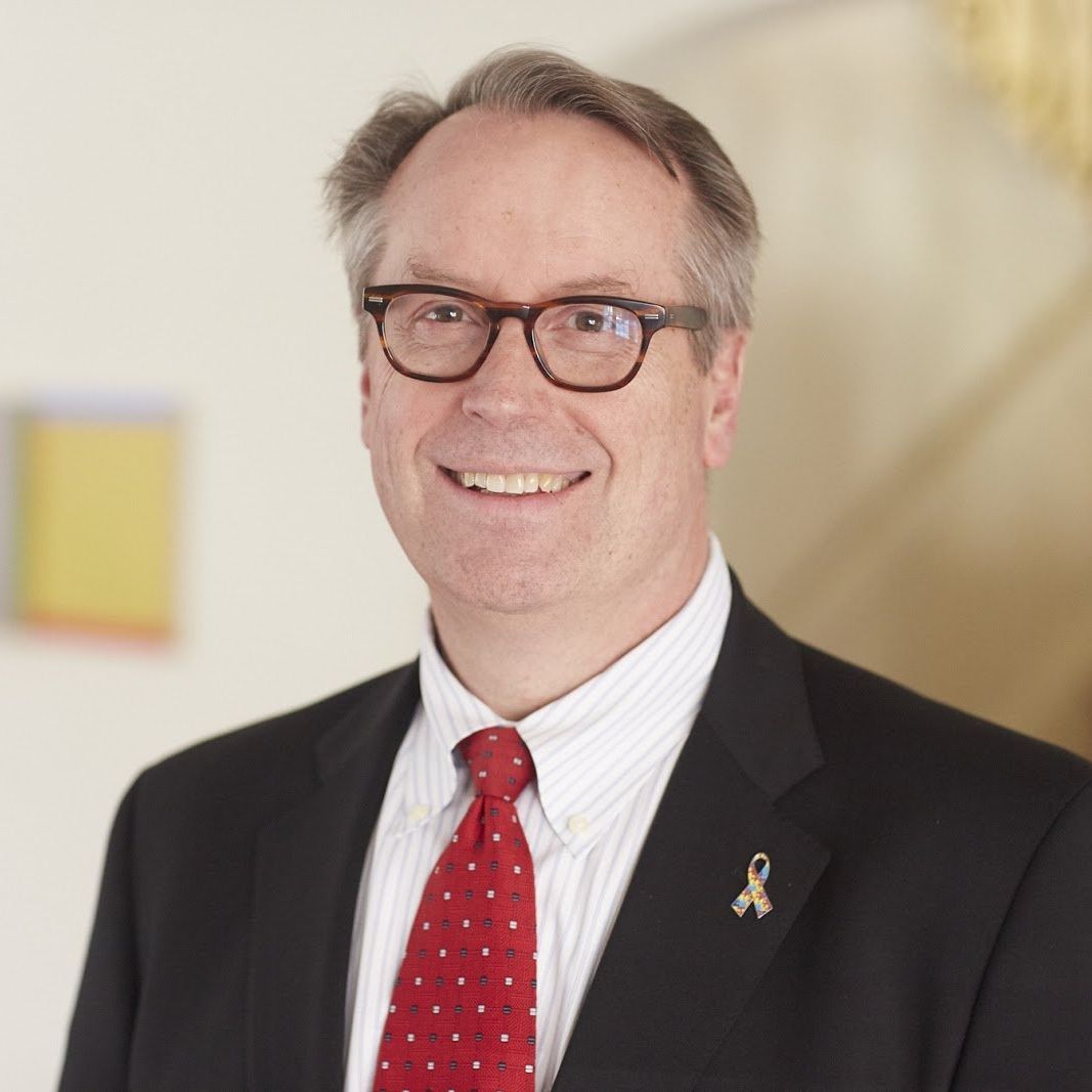 A man wearing glasses and a red tie is smiling for the camera