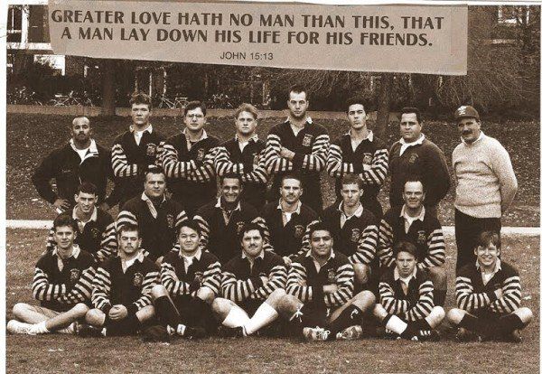 A group of men posing in front of a sign that says greater love hath no man than this