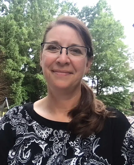 A woman wearing glasses and a black and white shirt is smiling for the camera.