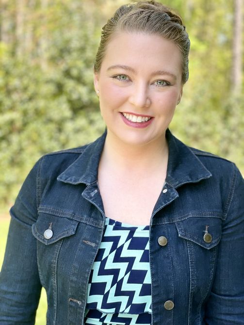 A woman wearing a denim jacket and a blue and white shirt is smiling for the camera.