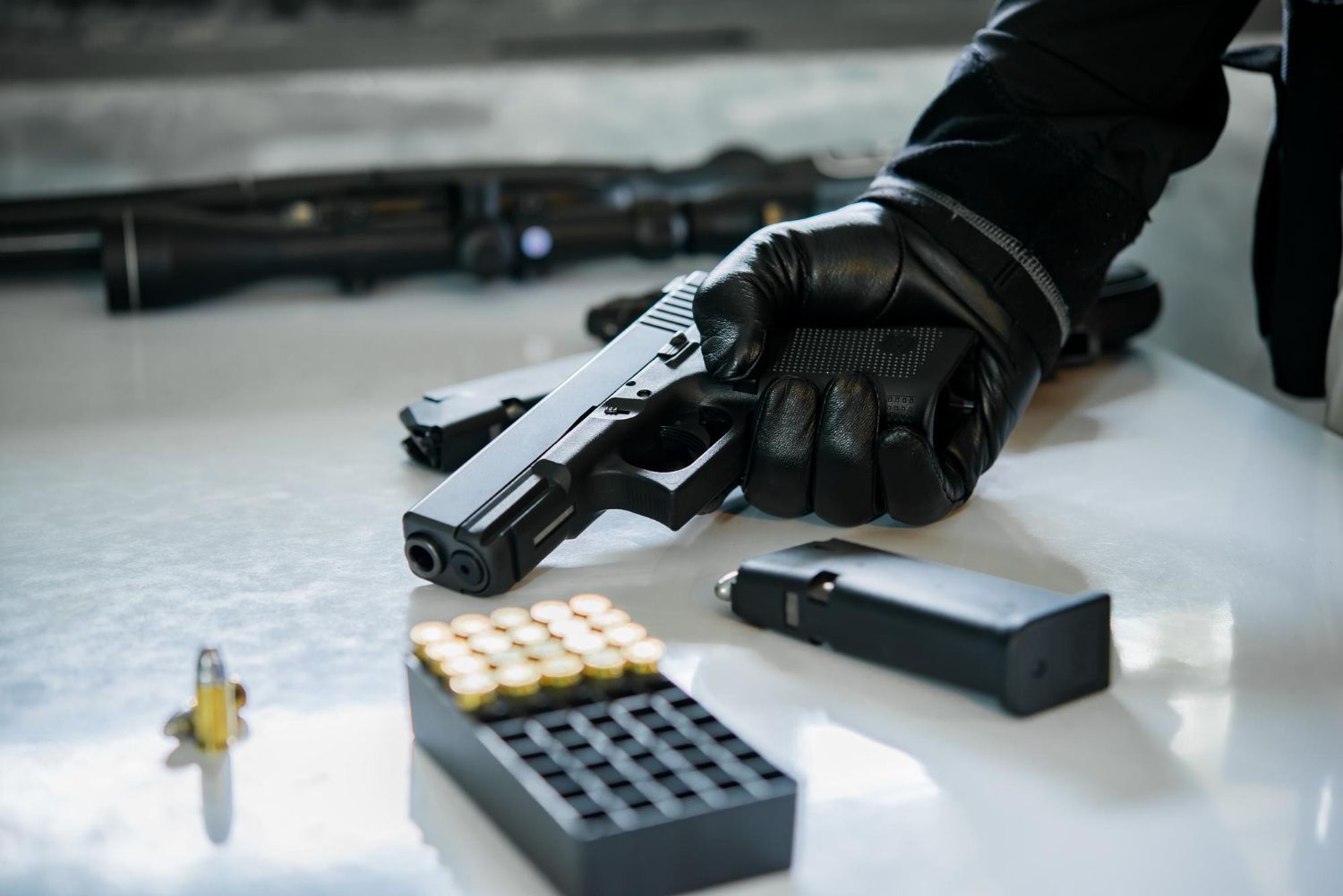 Gloved hand holding a handgun beside ammunition and a magazine on a table