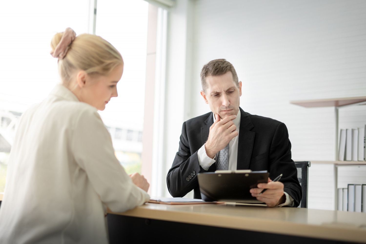 Two colleagues in a meeting, one taking notes while the other looks at a tablet