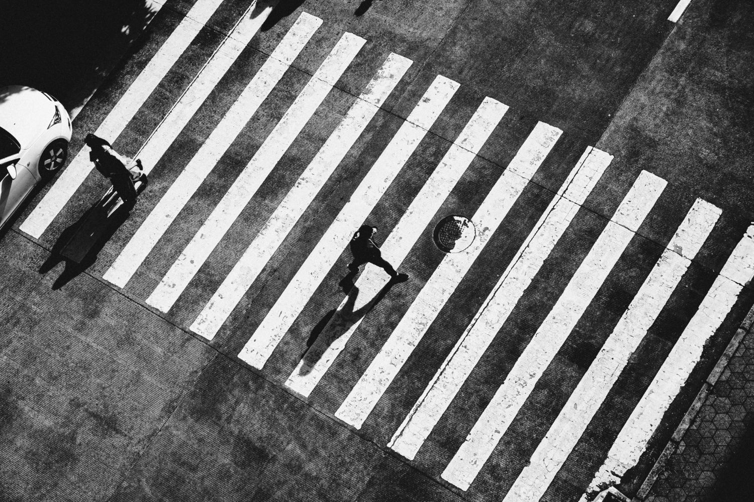 Pedestrian crossing with a person walking on white zebra stripes beside a parked scooter.
