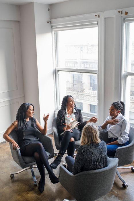 Small group in a bright office lounge having a seated discussion by large windows.
