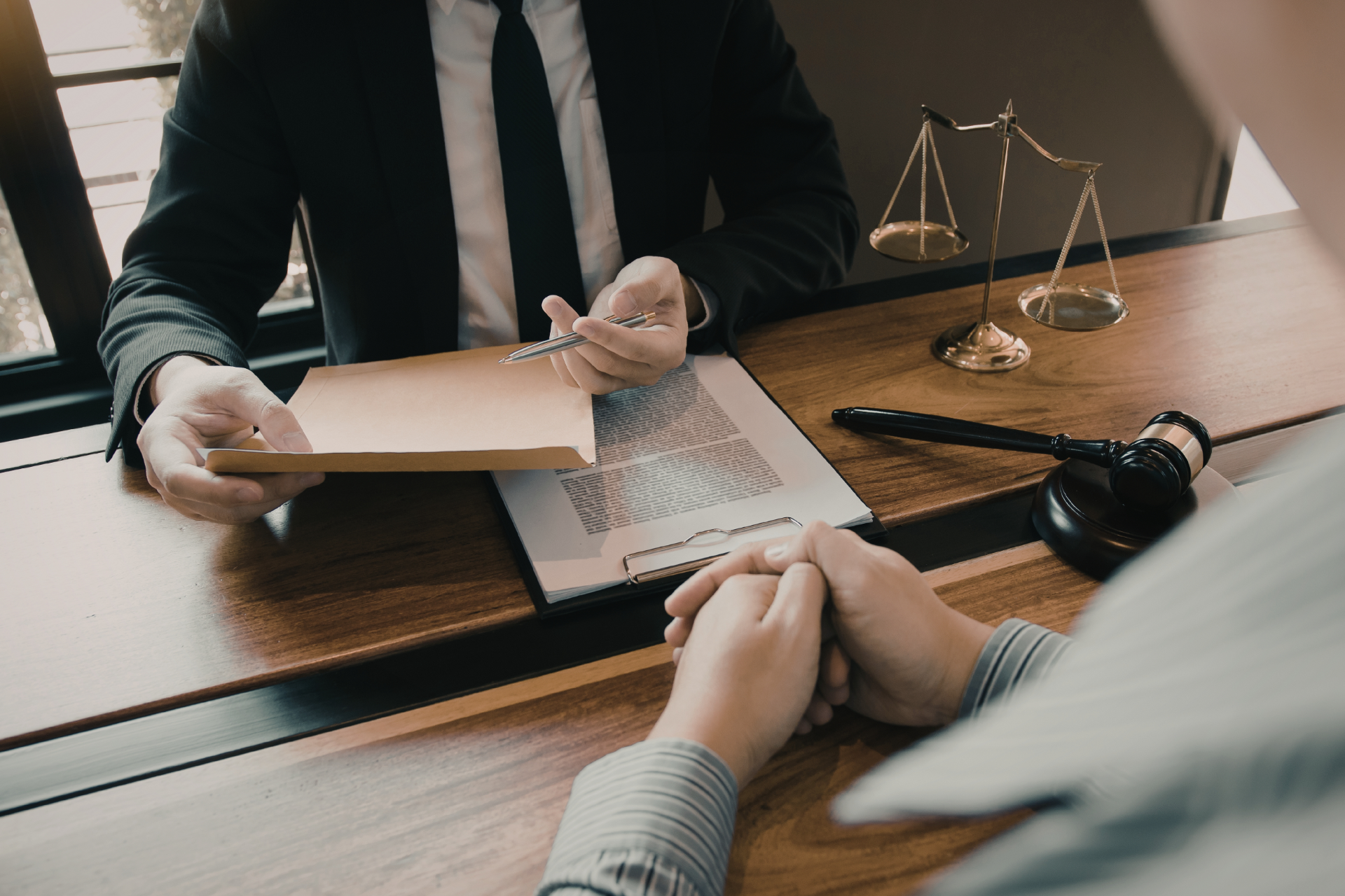 Two people discussing paperwork at a desk with a laptop, scales of justice, and a gavel.