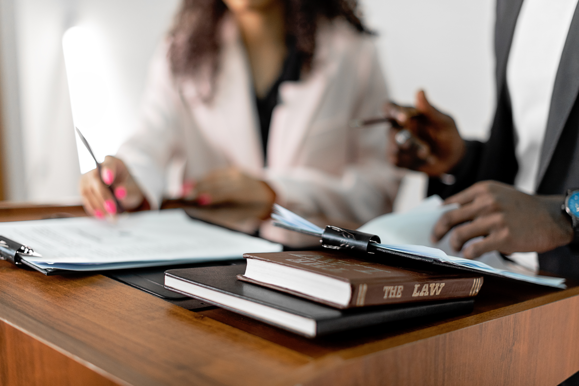 Two people discussing documents at a conference table with notebooks, a pen, and a tablet