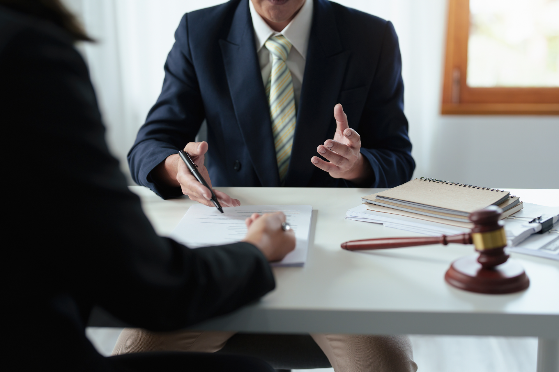 Two people in a lawyer’s office discuss a case at a desk with a gavel and documents.