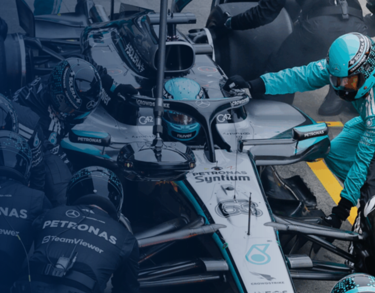 Formula 1 pit crew servicing a silver and black Mercedes car. Crew members in teal suits.