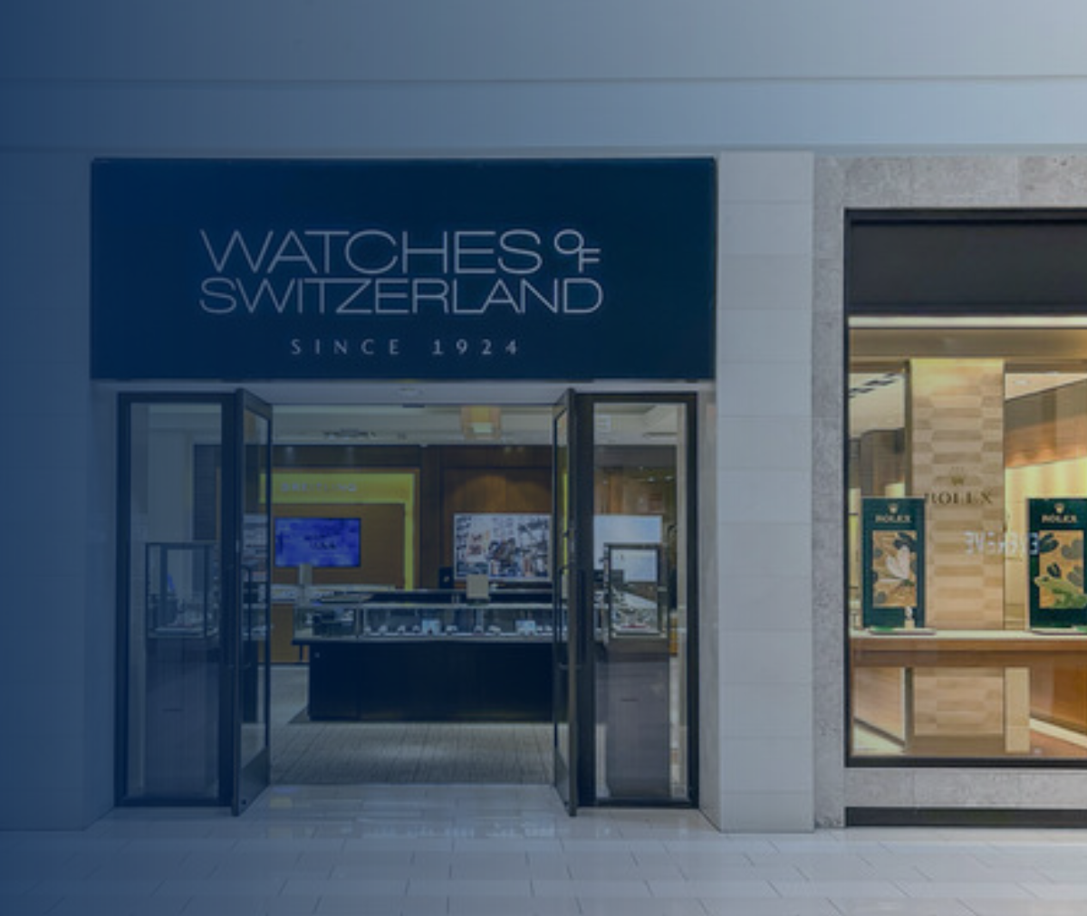 Watches of Switzerland store exterior with glass doors and display windows. Blue sign,