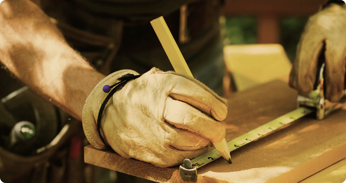 Close-up of hands using a pencil and ruler to measure wood on a workbench.