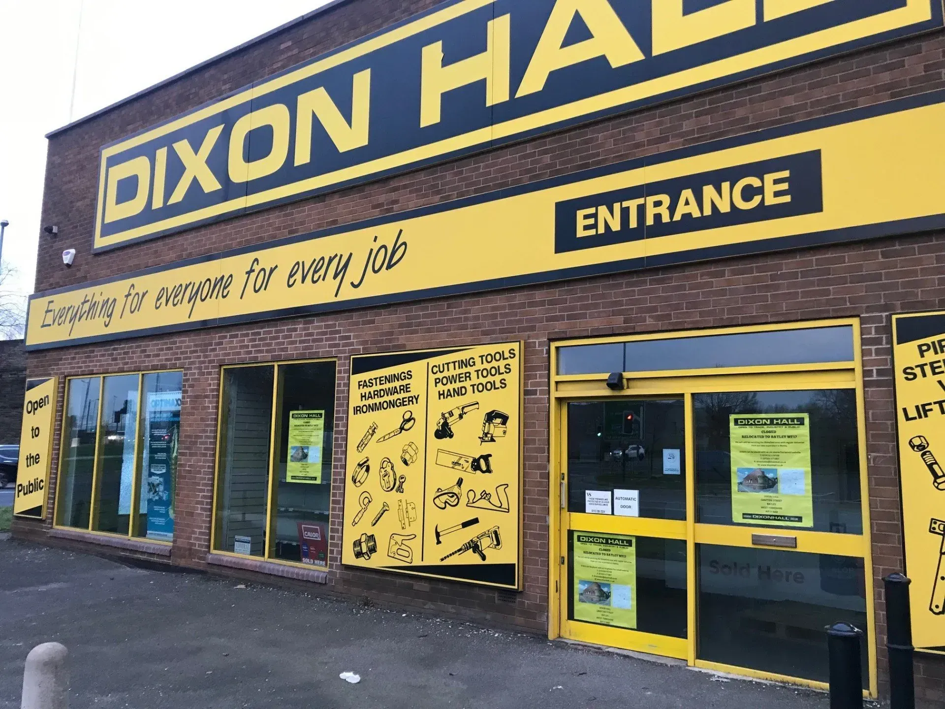 Exterior of Dixon Hall hardware store with yellow and black signage, brick facade, and glass windows.