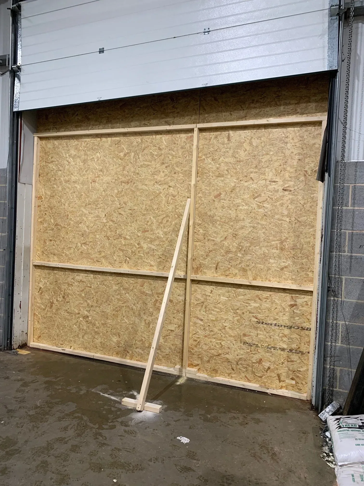 Garage door opening covered with wood panels. A long stick leans against the paneling on the inside.