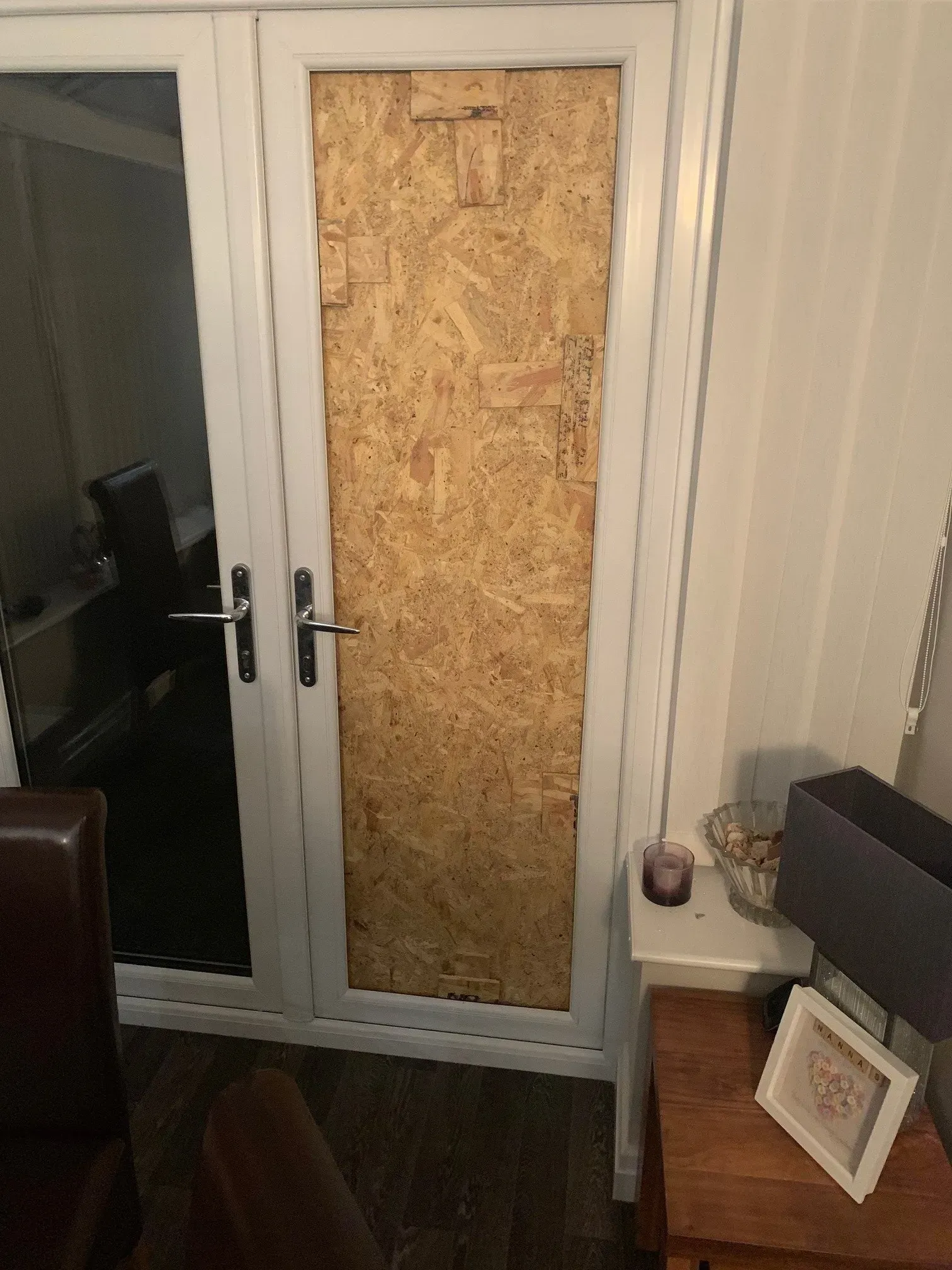 White french doors with one panel covered by wooden board, lit interior.